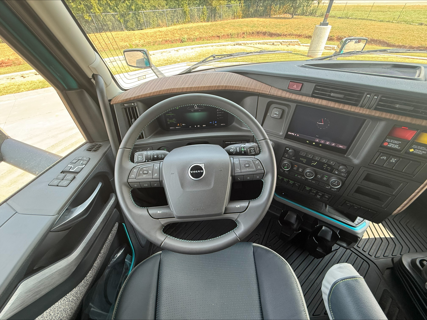 Volvo truck cab interior with steering wheel, dashboard, and control panel; visible steering wheel badge, digital gauge cluster, center console, and glass windows.