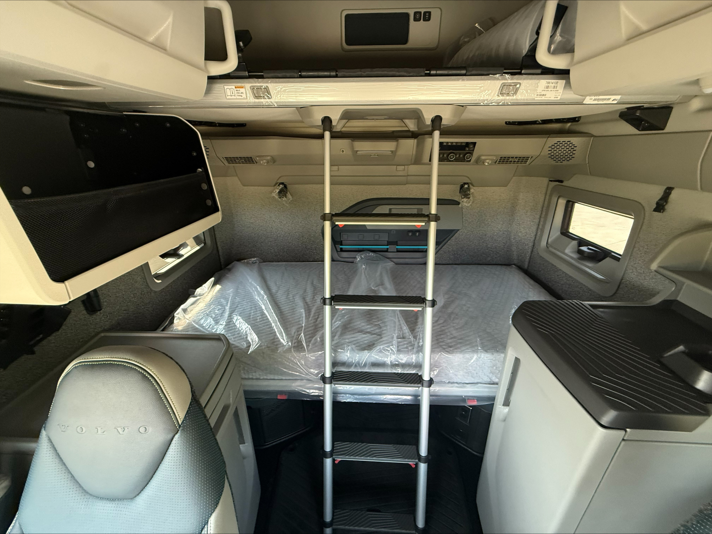 Volvo VNL cabin interior with upper bunk, ladder, and storage shelves; sleeper area visible with mattress still wrapped.
