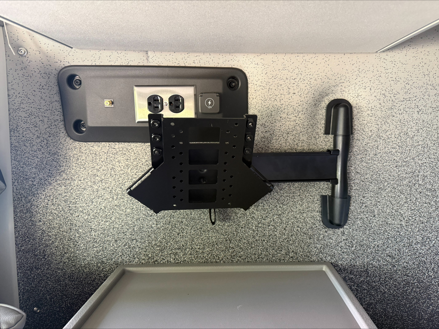 Rear view of a Volvo VNL64T860 dash area with a mounting bracket, electrical outlets, and a black laptop/monitor mount in the cab wall; rough speckled gray interior surface.