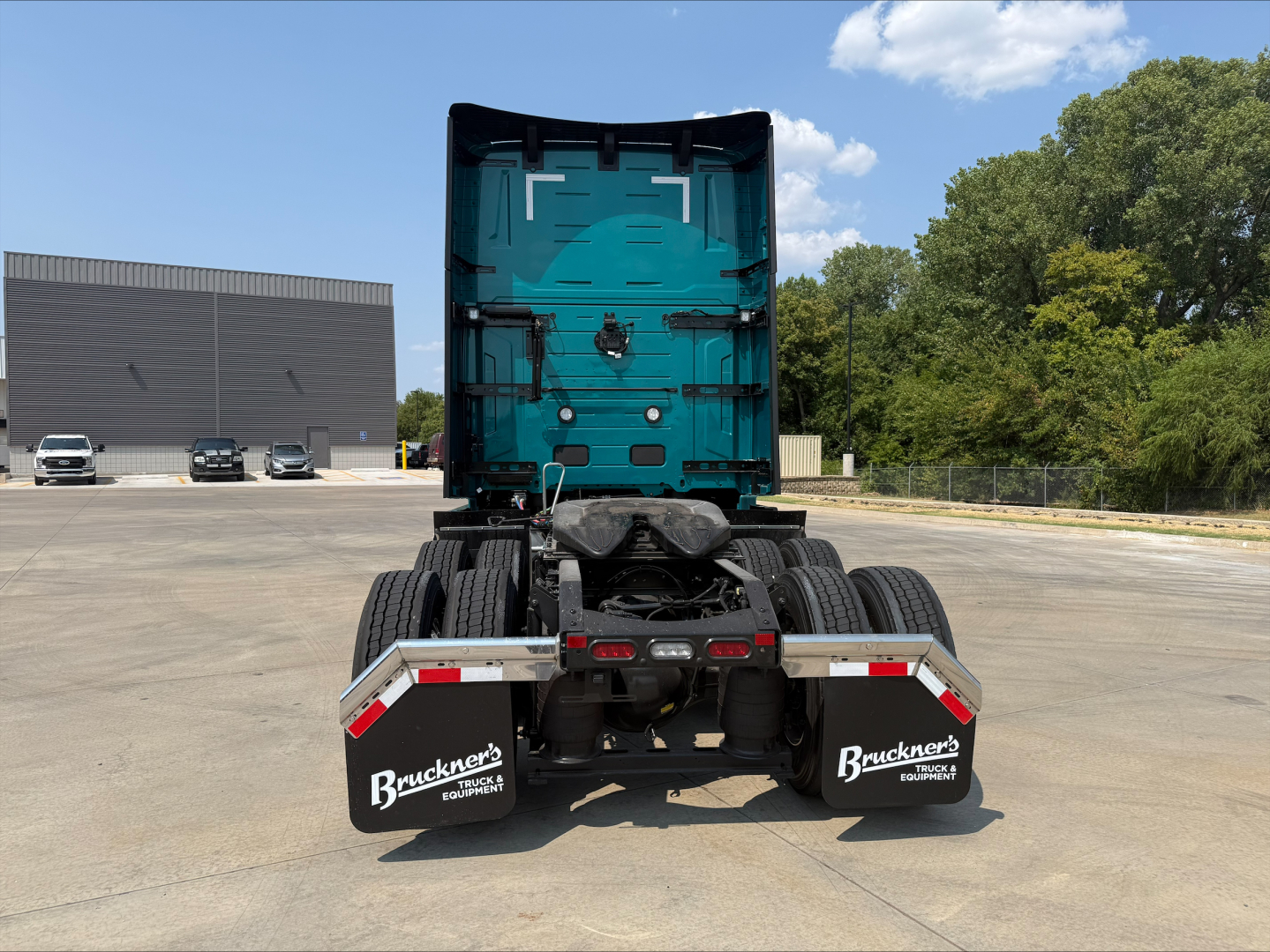 Truck rear view showing fifth wheel, rear tires, and mud flaps with Bruckner's Equipment branding; teal Volvo sleeper cab back wall visible.
