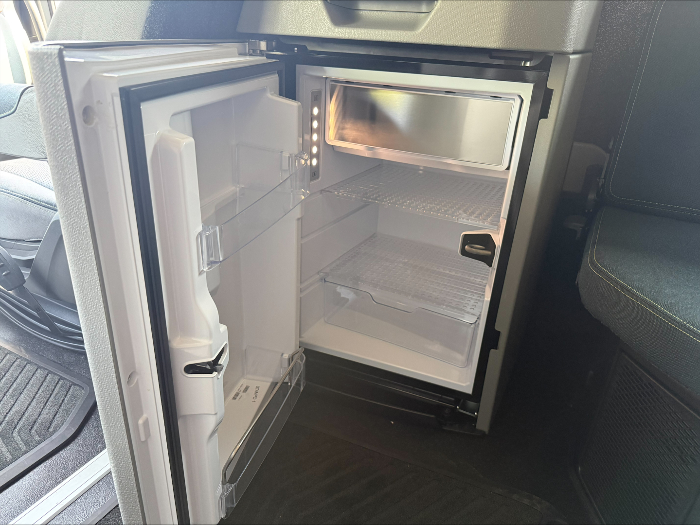 Mini refrigerator inside Volvo VNL64T860 sleeper cab with open door, showing empty shelves and small freezer compartment.