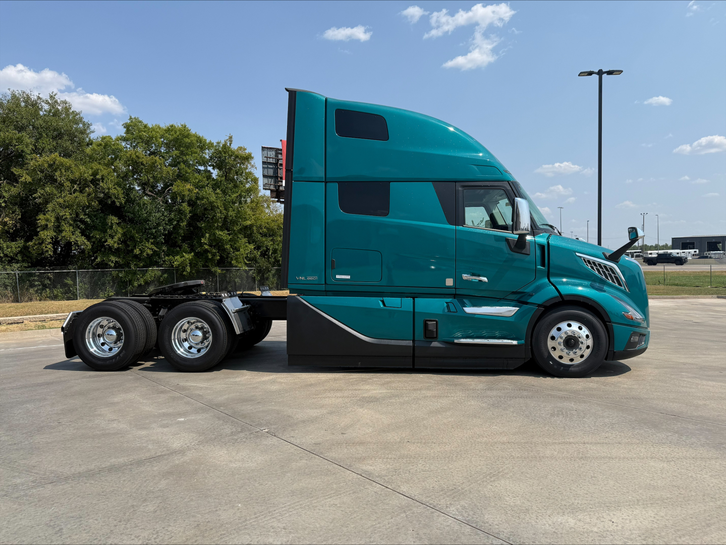 Volvo VNL64T860 truck side view showing teal exterior, sleeper cab, dual rear axles, chrome wheels, and fuel tanks.