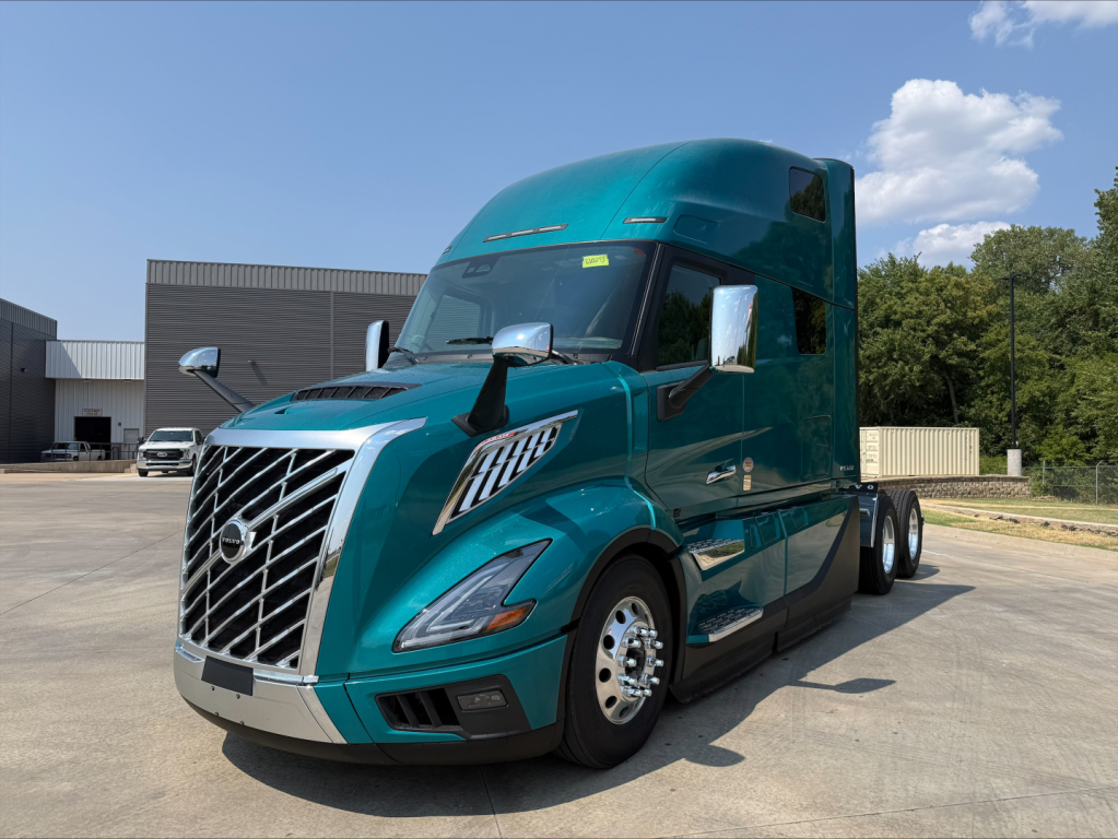Truck front view showing teal Volvo VNL64T860 sleeper cab with chrome grille and dual side mirrors.
