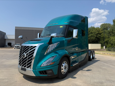 Truck front view showing teal Volvo VNL64T860 sleeper cab with chrome grille and dual side mirrors.