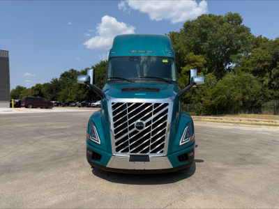 Front view of a turquoise 2027 Volvo VNL64T860 truck showing bold vertical grille, large headlights, side mirrors, and aerodynamic hood.