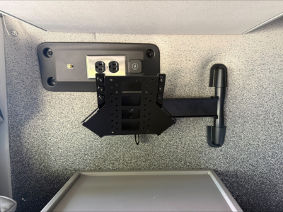 Rear view of a Volvo VNL64T860 dash area with a mounting bracket, electrical outlets, and a black laptop/monitor mount in the cab wall; rough speckled gray interior surface.
