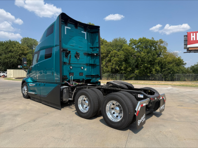 Teal Volvo VNL64T860 tractor in side/back view showing the rear of cab, dual rear axles, chrome wheels, and bumper pieces with mud flaps.