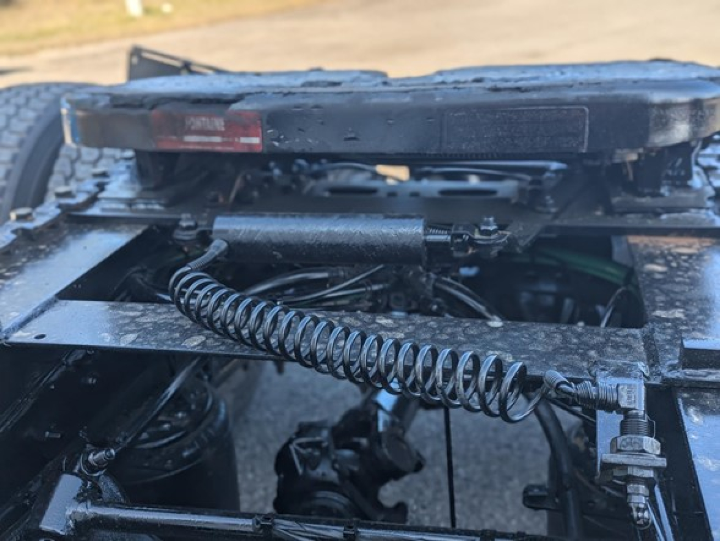 Freightliner Cascadia 126 truck chassis cab showing suspension linkage and coil spring undercarriage with hydraulic lines and frame components.