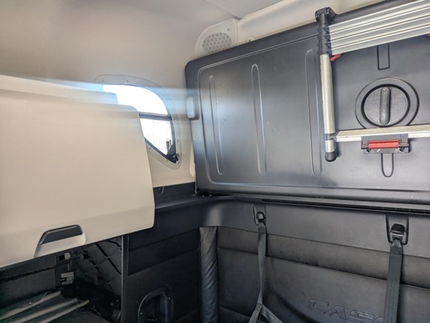 Cab interior of a Freightliner Cascadia 126 sleeper showing storage cabinet with latch and paneling, window view, and seat area.