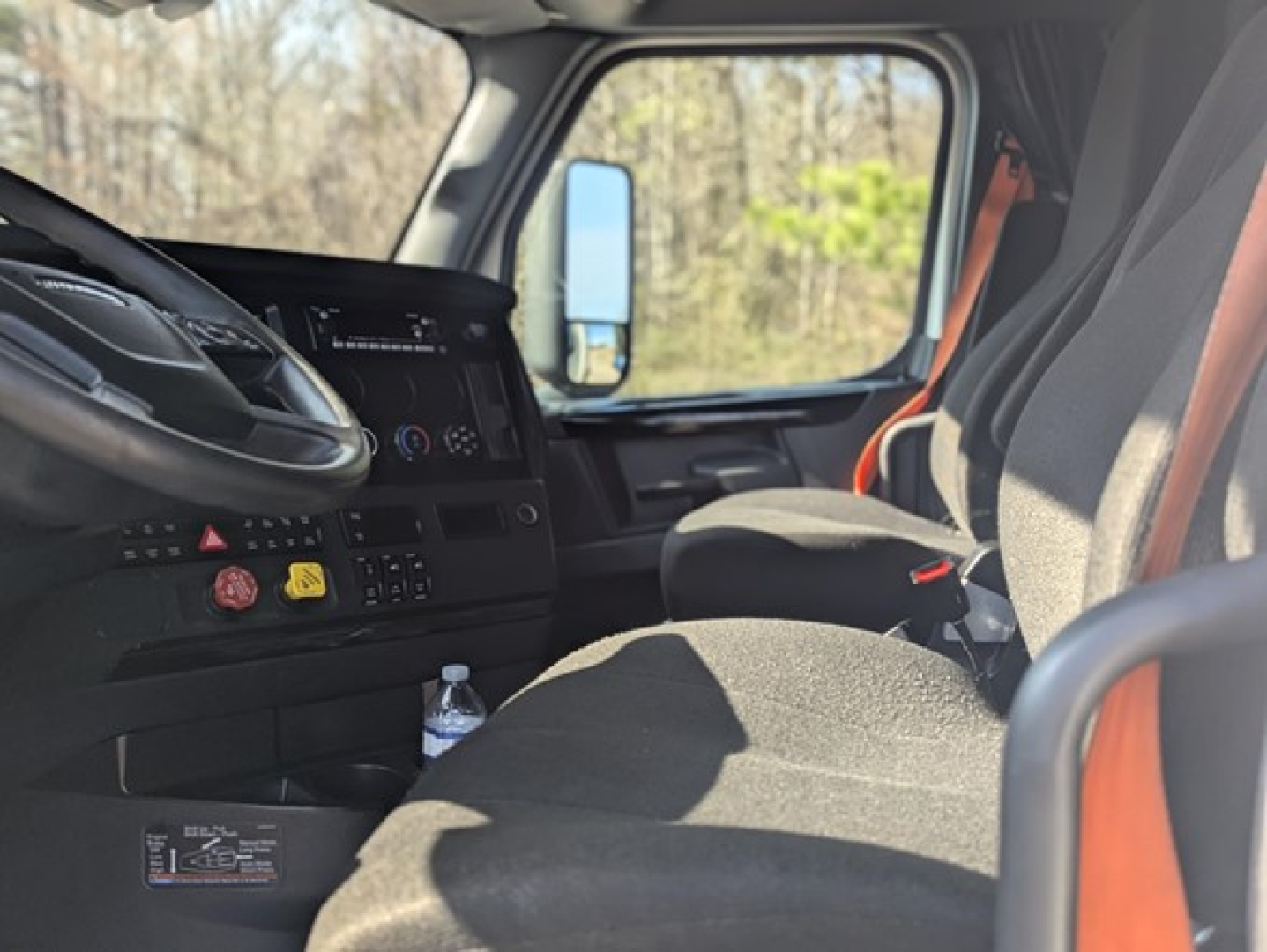 Cab interior of a 2023 Freightliner Cascadia 126 showing steering wheel, dashboard, seat, and window with natural light.