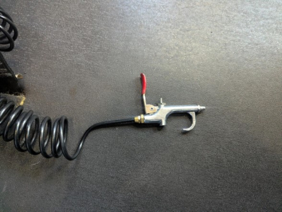 Tooling with coiled air line and trigger handle, mounted on a metallic surface.
