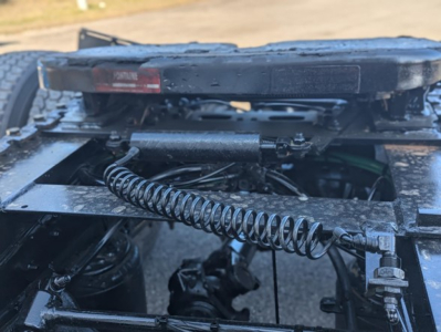 Freightliner Cascadia 126 truck chassis cab showing suspension linkage and coil spring undercarriage with hydraulic lines and frame components.