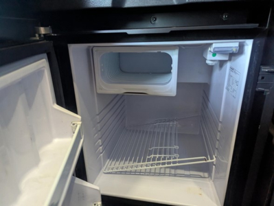Fridge/freezer in truck cab showing empty interior and small freezer section at top right.