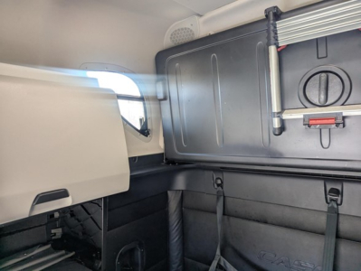 Cab interior of a Freightliner Cascadia 126 sleeper showing storage cabinet with latch and paneling, window view, and seat area.