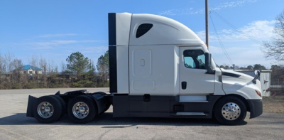 Truck side profile showing 2023 Freightliner Cascadia 126 sleeper tractor with white cab and black chassis, tandem rear axles, daytime parking lot.