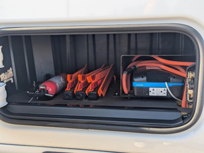 Tractor-trailer sleeper truck storage bay showing a blue Jump starter with red cables and an orange tool/parts tray.