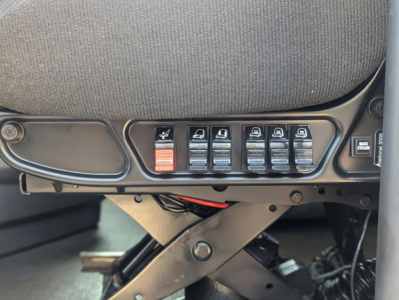 Tractor truck cab interior switch panel with multiple seat heater/power switches and a red emergency switch, part of Freightliner Cascadia 126 dashboard view.