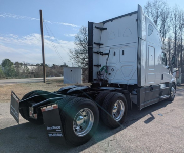 Freightliner Cascadia 126 tractor from rear side showing sleeper cab and dual rear axles with fifth wheel and mud flaps.