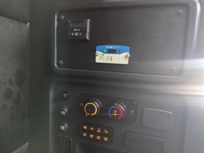 Dash panel of Freightliner Cascadia showing control switches and a blue/white device mounted in overhead area.