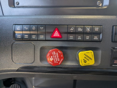 Truck dashboard controls with labeled buttons: slr/dome, ambt light, dome light, light test, hazard triangle, utility light, atc spin, low idle, eng shdn, parking brake yellow knob, red red knob with 'TRAILER AIR' text.