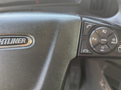 Steering wheel of a Freightliner Cascadia showing part of the dash with control buttons and a 'FREIGHTLINER' badge.