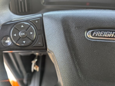Cab view of Freightliner Cascadia steering wheel with control pad and Freightliner badge visible.