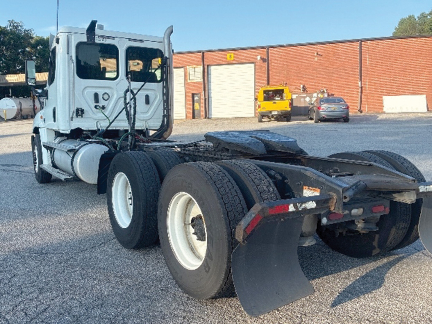 Tractor truck chassis with cab and dual rear axles showing fifth wheel and mud flaps; Freightliner Cascadia125 style cab in light blue, visible in an outdoor lot.