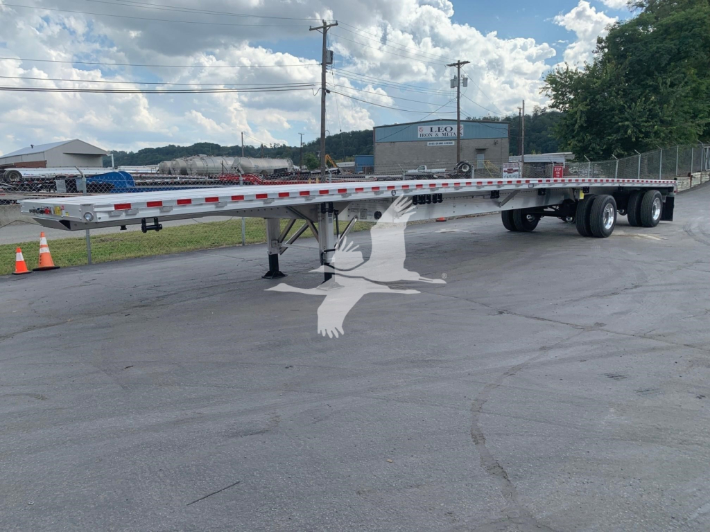 Flatbed trailer showing Maximer-style flatbed with tandem axles and support legs, chrome safety rails and reflective tape along the rails.