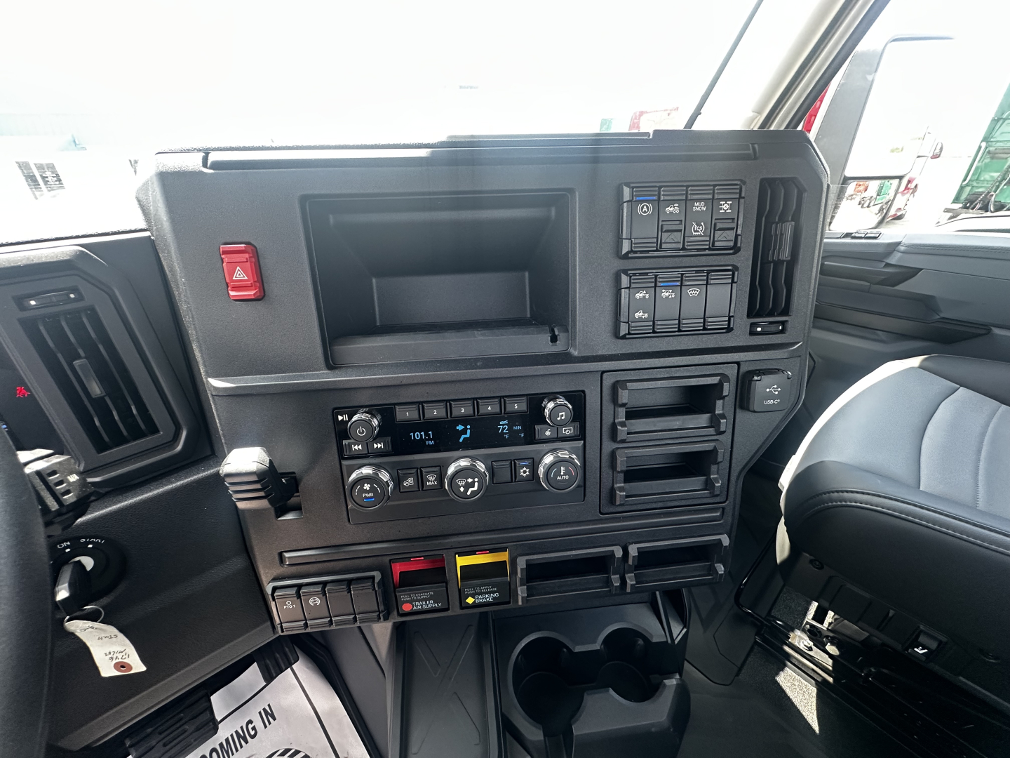 Truck dashboard area of a 2027 Mack AN64T cab showing steering wheel, center console with air controls, switches, and storage compartments.