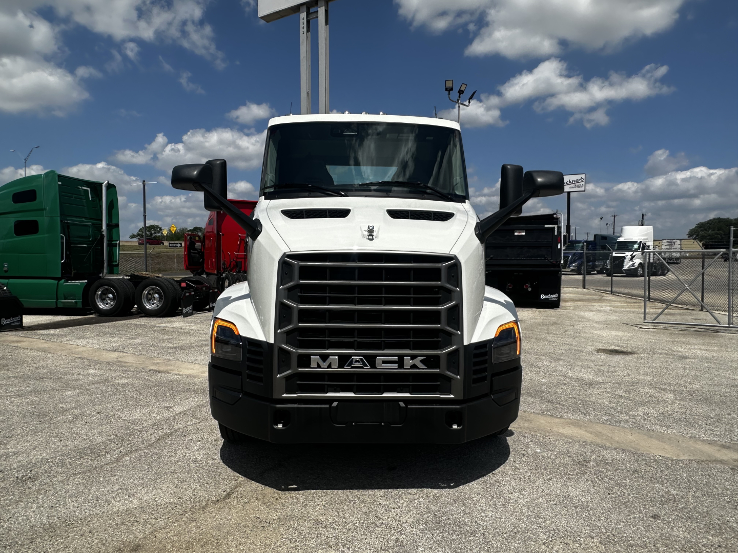 Front view of white 2027 Mack AN64T truck in a dealership lot with other trucks in background.