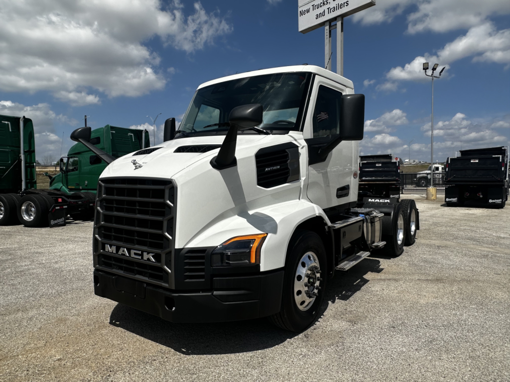 White 2027 Mack AN64T conventional daycab truck in dealership lot, front three-quarter view showing grille, headlights, Mack emblem, cab mirrors, and front tires.