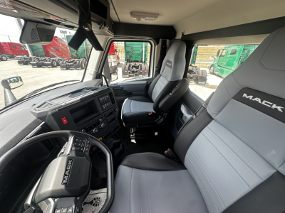 Interior view of a 2027 Mack AN64T cab, showing steering wheel, driver seat, and front bench; dashboard with controls and a passenger seat with Mack branding.