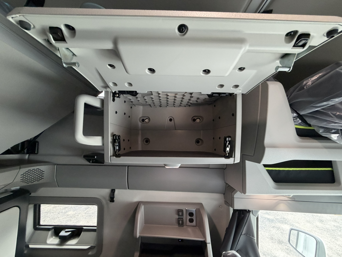 Dashboard area of a new Volvo VNL truck showing overhead storage box opened, center console with control panel, and storage compartments.