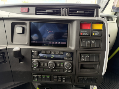 Dashboard view of a Volvo VNL64T860 interior showing control panels, screen, and colored warning buttons.