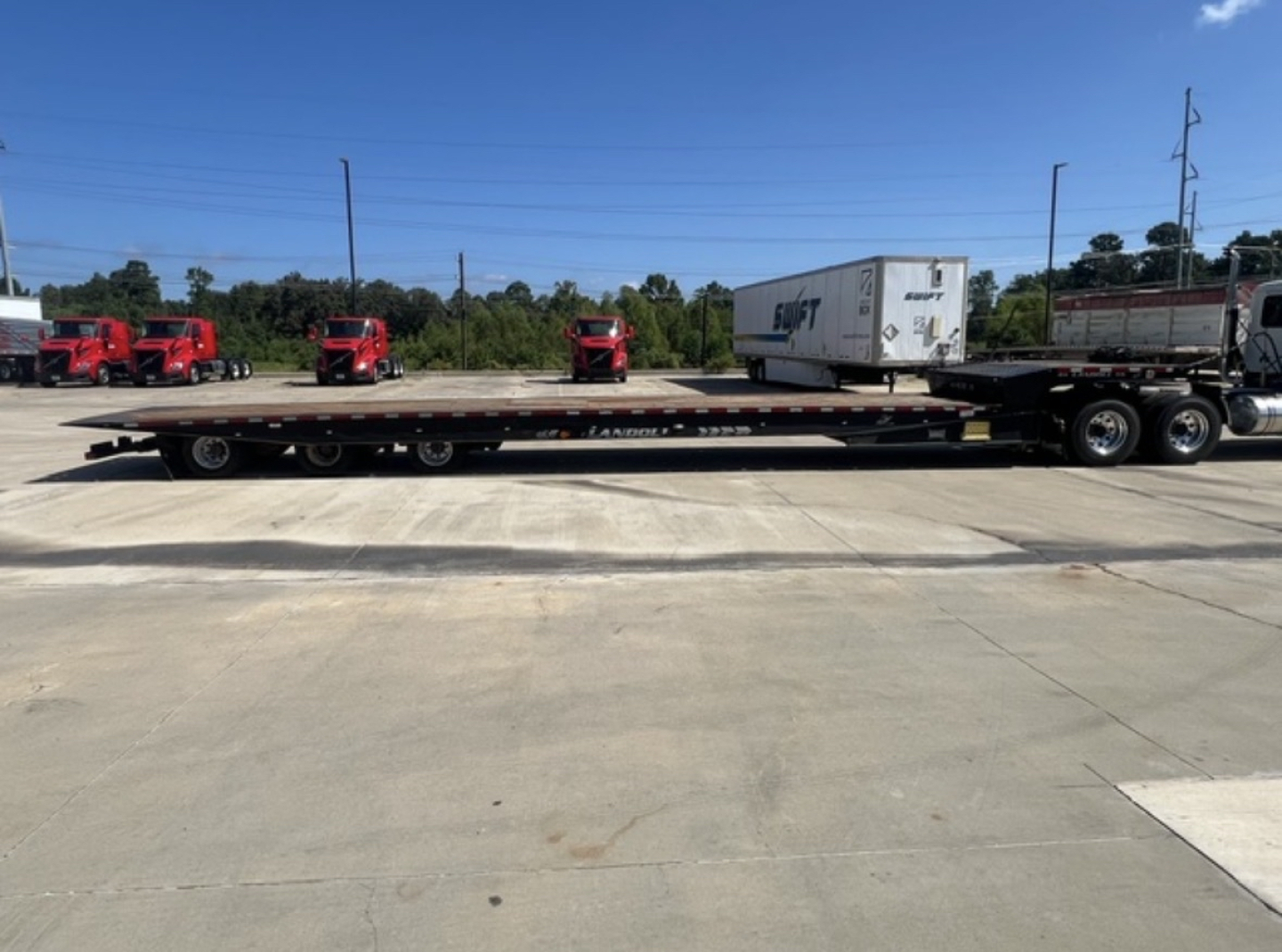2018 Landoll 455 traveling axle trailer showing flatbed with a white trailer on top and multiple red trucks in background.