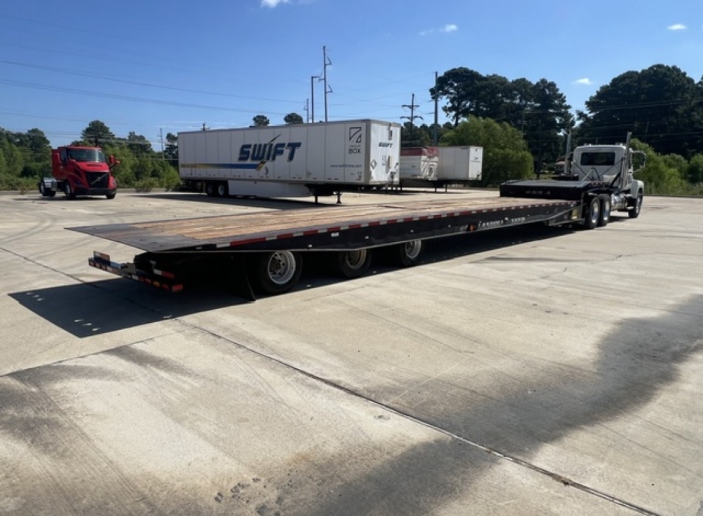 2018 Landoll 455 traveling axle trailer with extended lowboy and cab tractor in background, side view showing long flatbed and multiple axles.