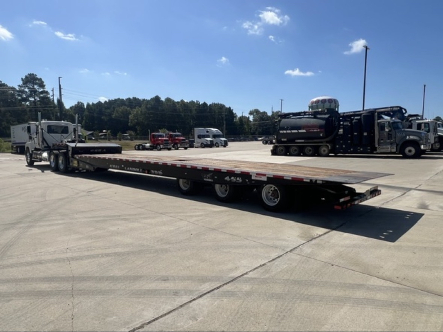 Landoll 455 trailer in a parking lot showing a long flatbed with multiple axles, cab, and other equipment in the background.