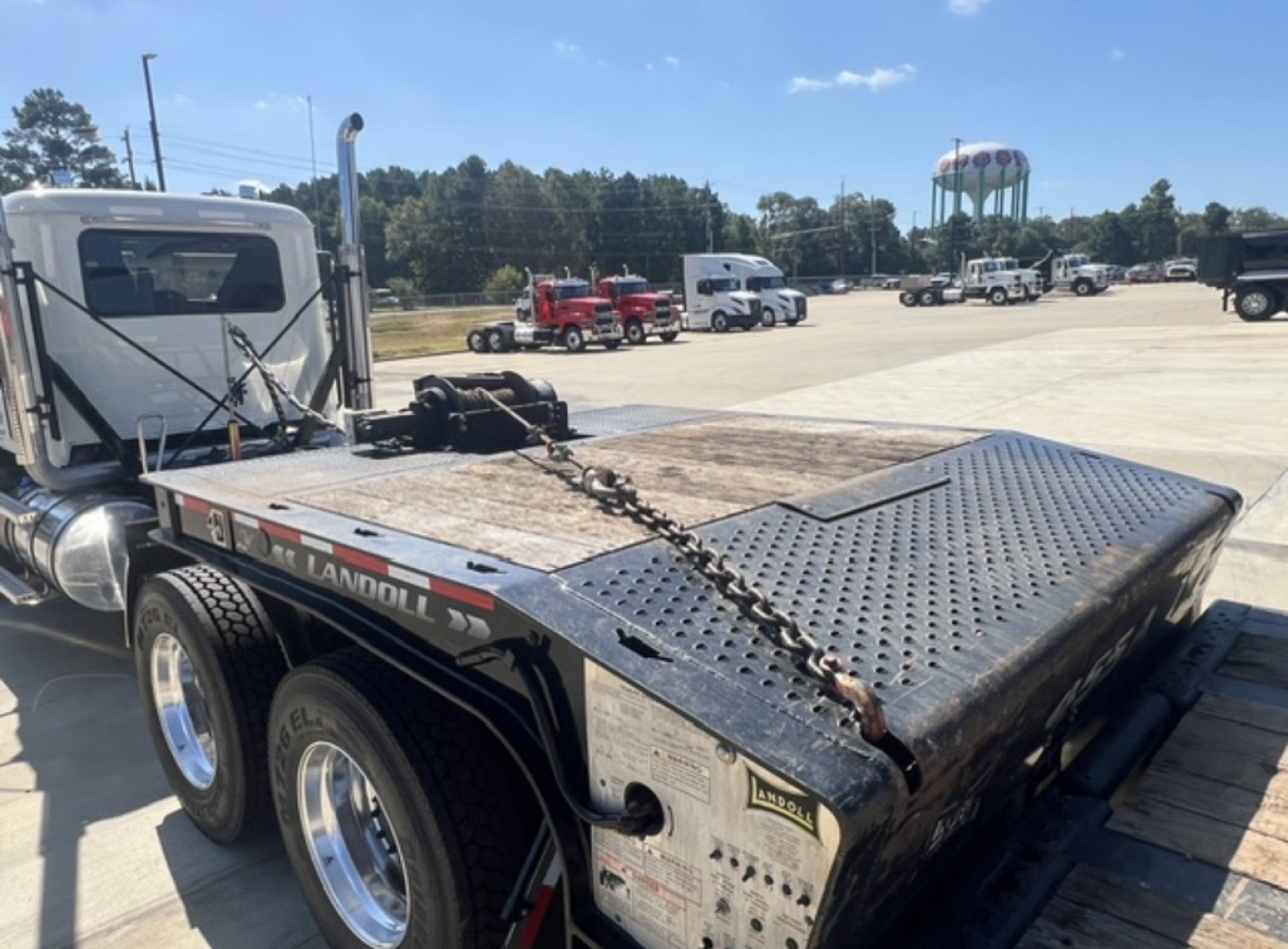 Trailer deck on Landoll 455, metal perforated surface, chains, and side rails visible; voltage and branding stickers present on the side; front cab of truck at left.
