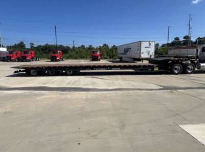 2018 Landoll 455 traveling axle trailer showing flatbed with a white trailer on top and multiple red trucks in background.