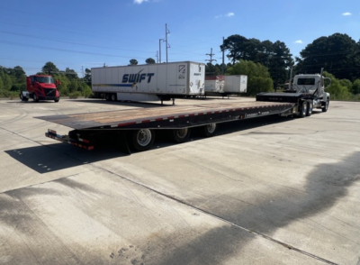 2018 Landoll 455 traveling axle trailer with extended lowboy and cab tractor in background, side view showing long flatbed and multiple axles.