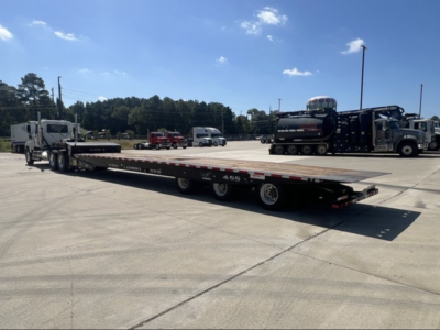 Landoll 455 trailer in a parking lot showing a long flatbed with multiple axles, cab, and other equipment in the background.