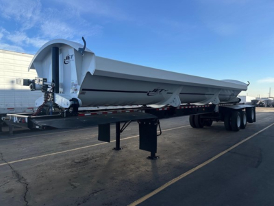 Jet trailer with spread dump body showing Jet logo on front and side, white with black stripe, trailer in parking lot.