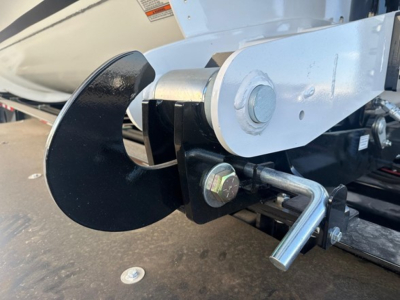 Trailer hitch assembly showing a black curved blade against metallic bracket and bolt with a hex nut and a small L-shaped ratchet handle visible.