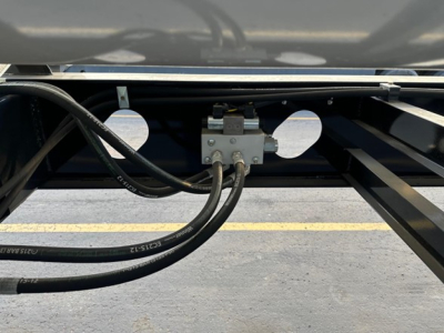 Trailer component with hydraulic hoses and mounting bracket showing two circular cutouts in the frame.