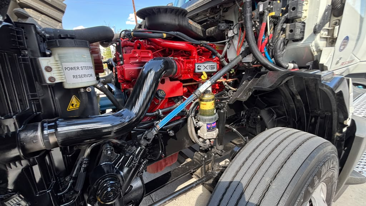 International LT625 engine bay showing red engine block, black intake ducts, coolant reservoir labeled POWER STEER RESERVOIR, and wiring harnesses.