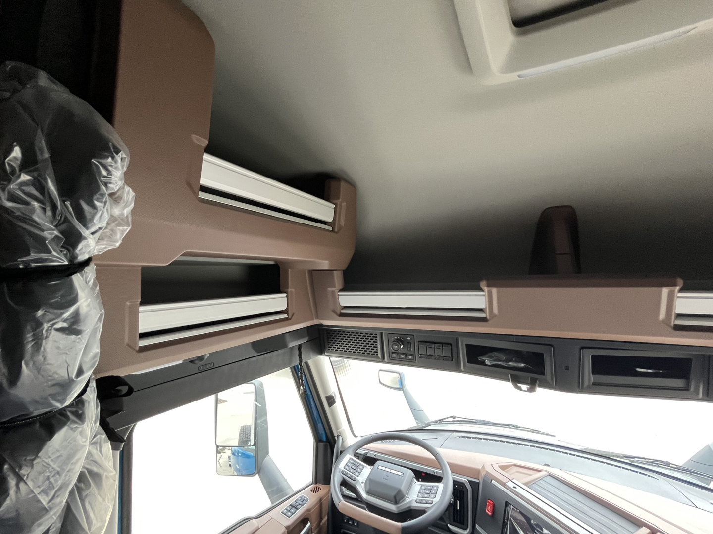 Interior of a Mack AN64T64 sleeper cab showing dashboard, steering wheel, overhead bunk storage, and driver seat.