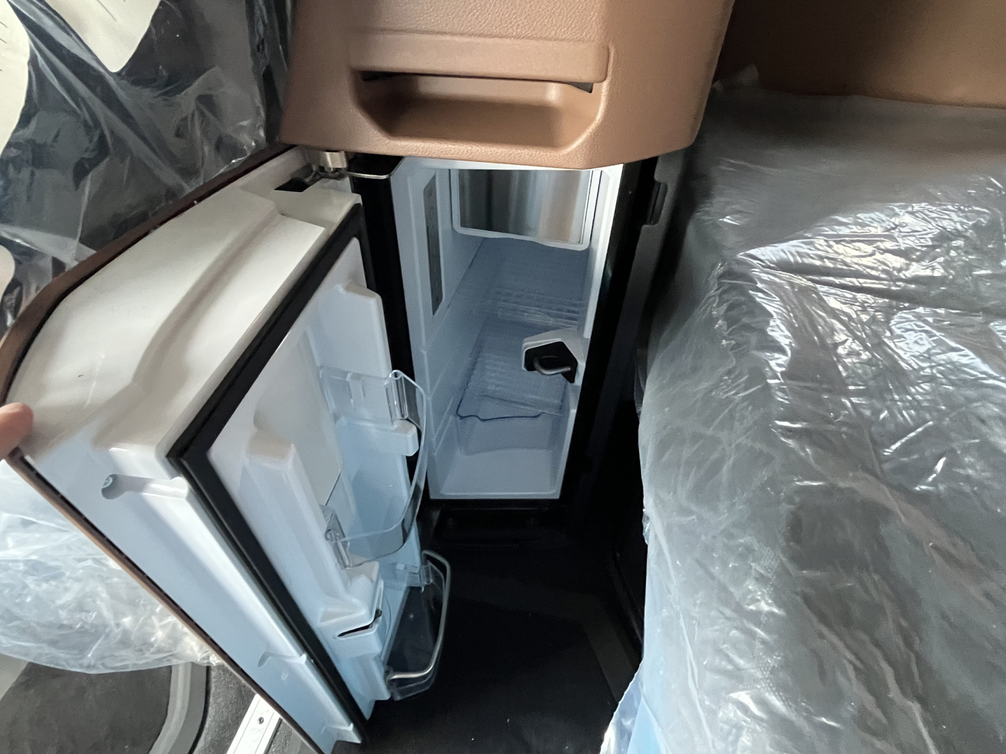 Truck interior: open mini-bar style refrigerator or storage box in cab with light interior, door open showing shelves.