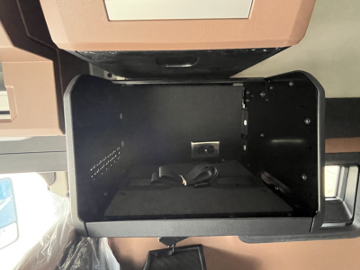 Truck interior storage compartment under dash open showing empty cavity with wiring and mounting points.