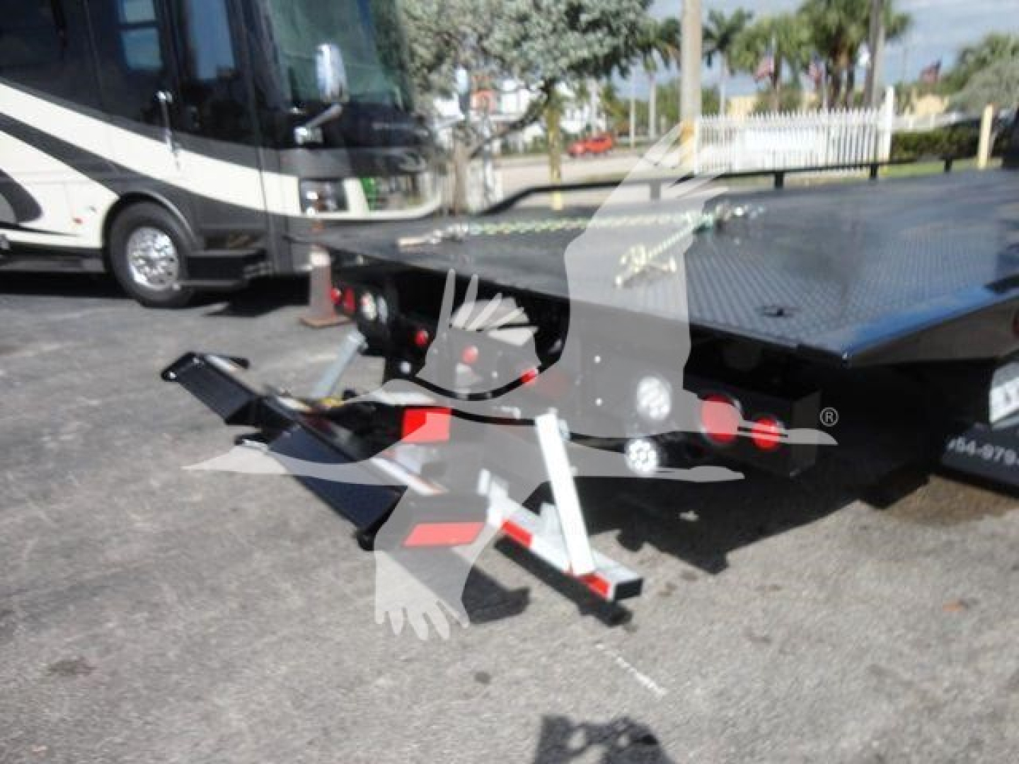 Vehicles in a dealership lot featuring a flatbed rollback tow truck with a black and white bus in the background.