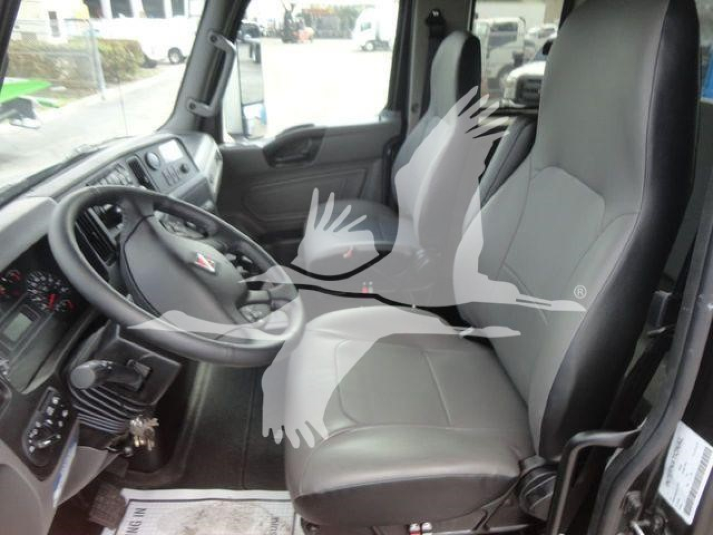 Interior of a new 2027 International MV truck cab showing driver and passenger seats, steering wheel, and dashboard area with gray seating.